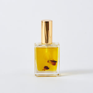 harmonious body oil, back of bottle, yellow liquid coloured oil with 3 red rose petals floating, gold atomiser lid.