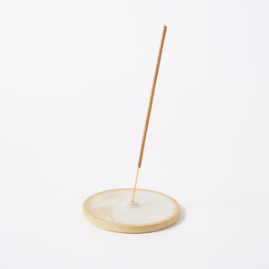round shaped ceramic incense holder in white/cream colour with incense stick standing tall