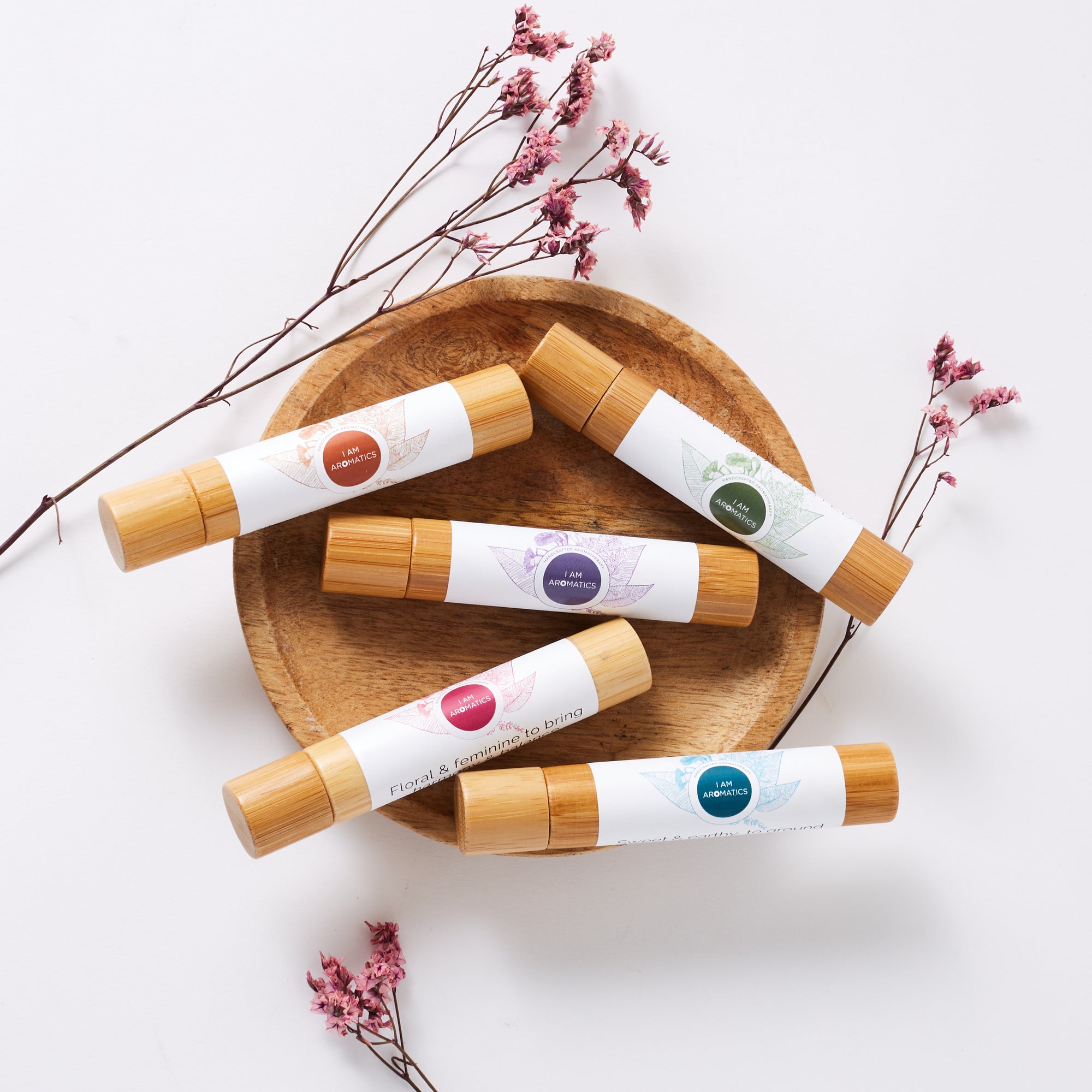 Wooden bowl with 5 bamboo rollers laying inside, coloured botanical logos. botanical twigs in background