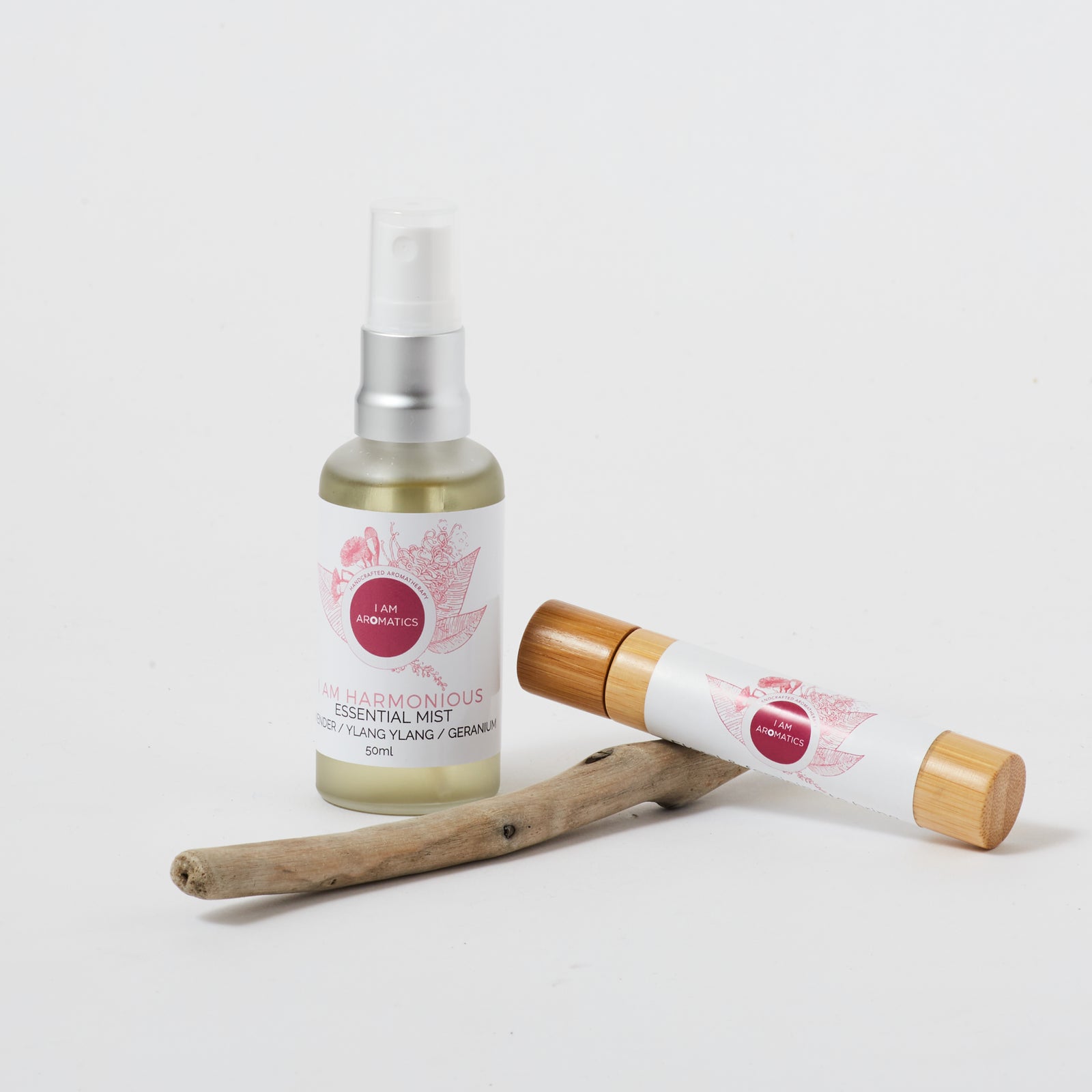 harmonious 50ml essential mist with matt silver atomiser, pink logo and font, pictured with a piece of driftwood and harmonious bamboo natural perfume roller 10mls