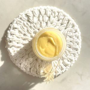 i am nourished face cream, jar opened to view buttercup coloured face cream, jar sitting on a white round face cloth wiht a botanical twig